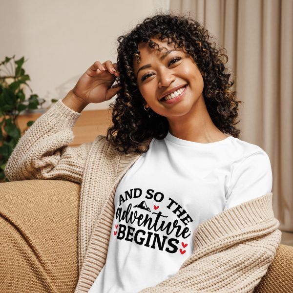 Smiling woman wearing 'adventure begins' shirt indoors.